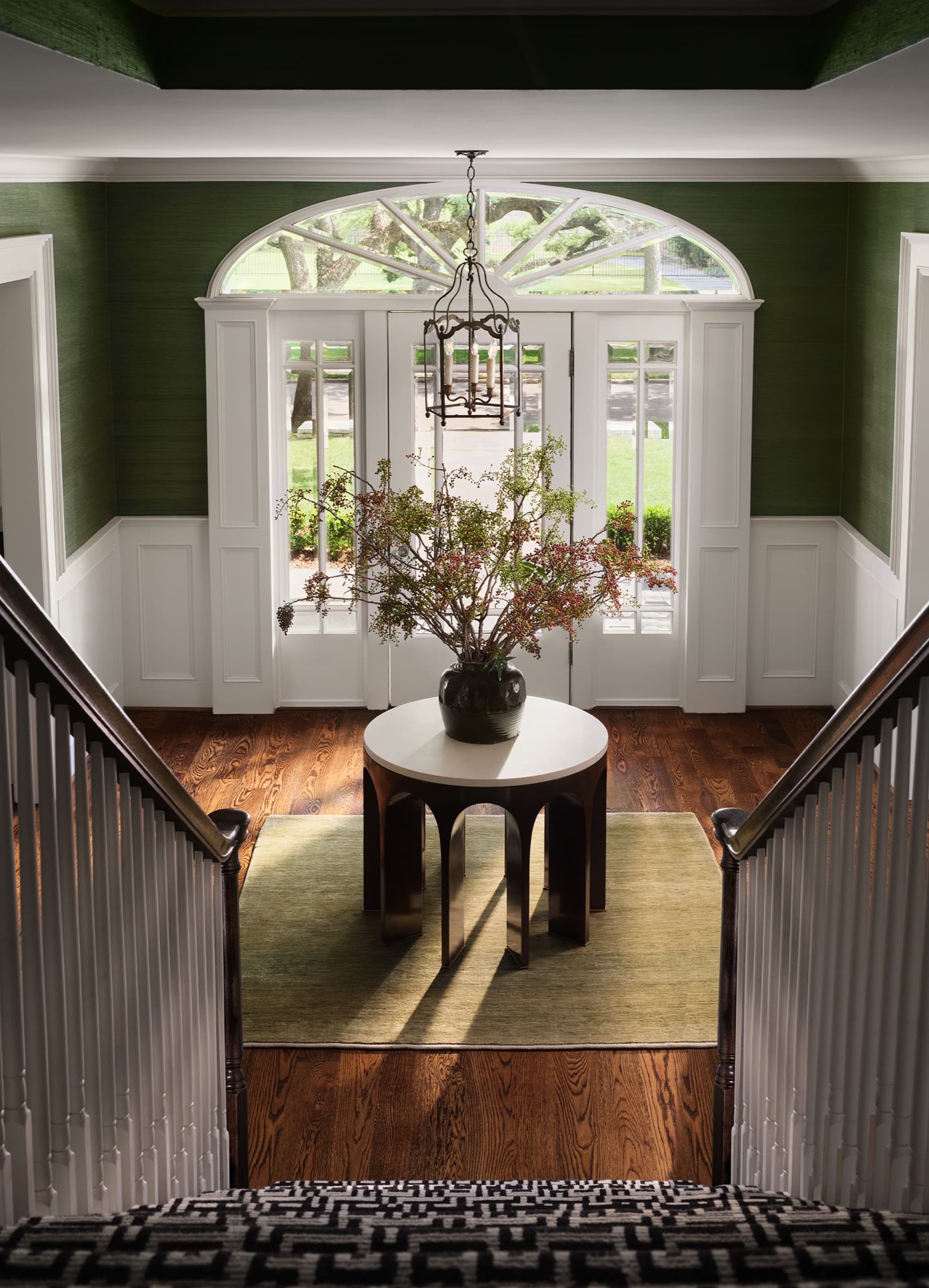 The Houston stair hall uses crisp millwork, saturated green walls, and dark rail detail to anchor arrival.