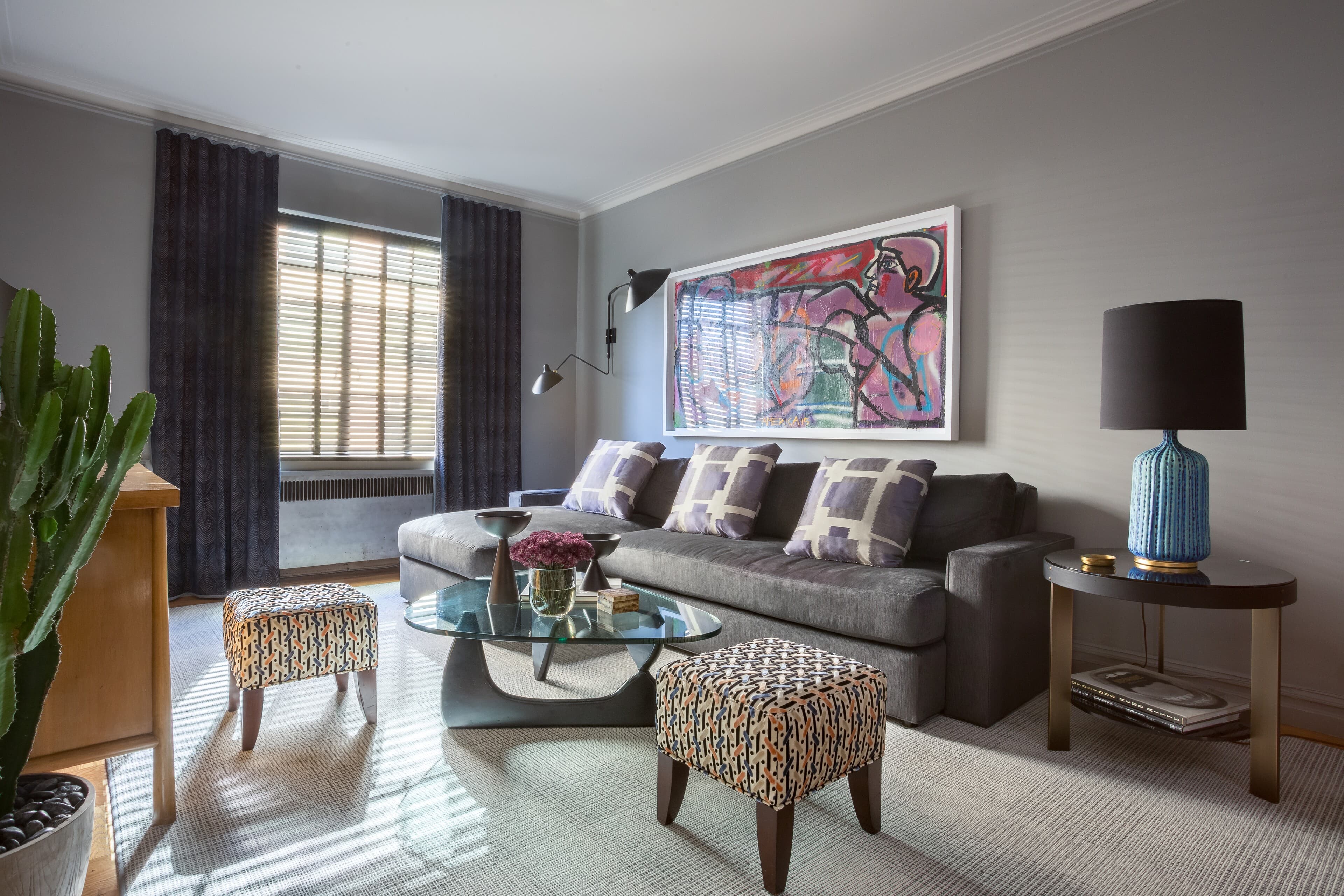 The living-room hero pairs a charcoal sofa, patterned ottomans, warm wood, and expressive art.