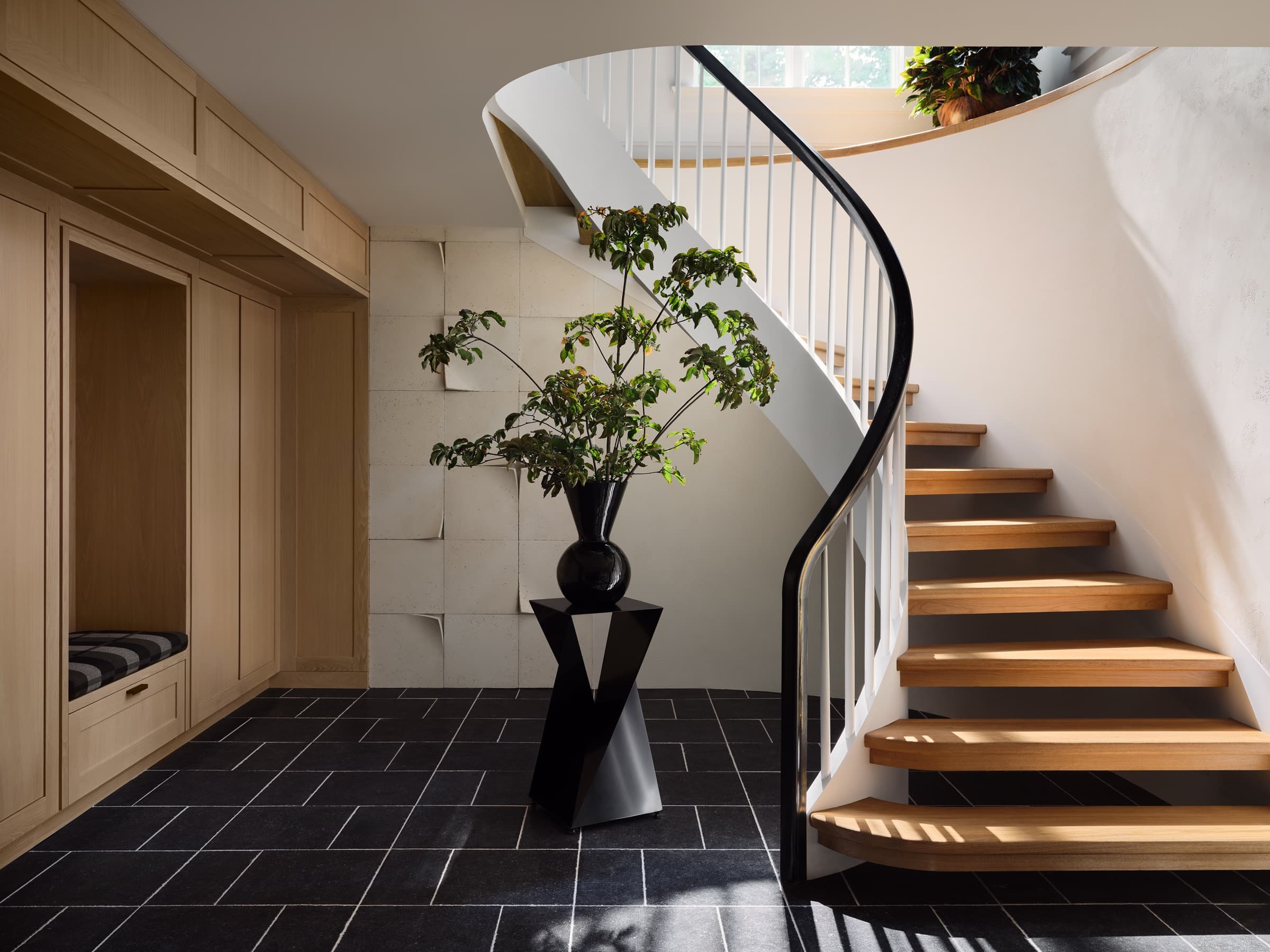 Curved staircase with oak millwork, stone wall, black handrail, and sculptural art placement